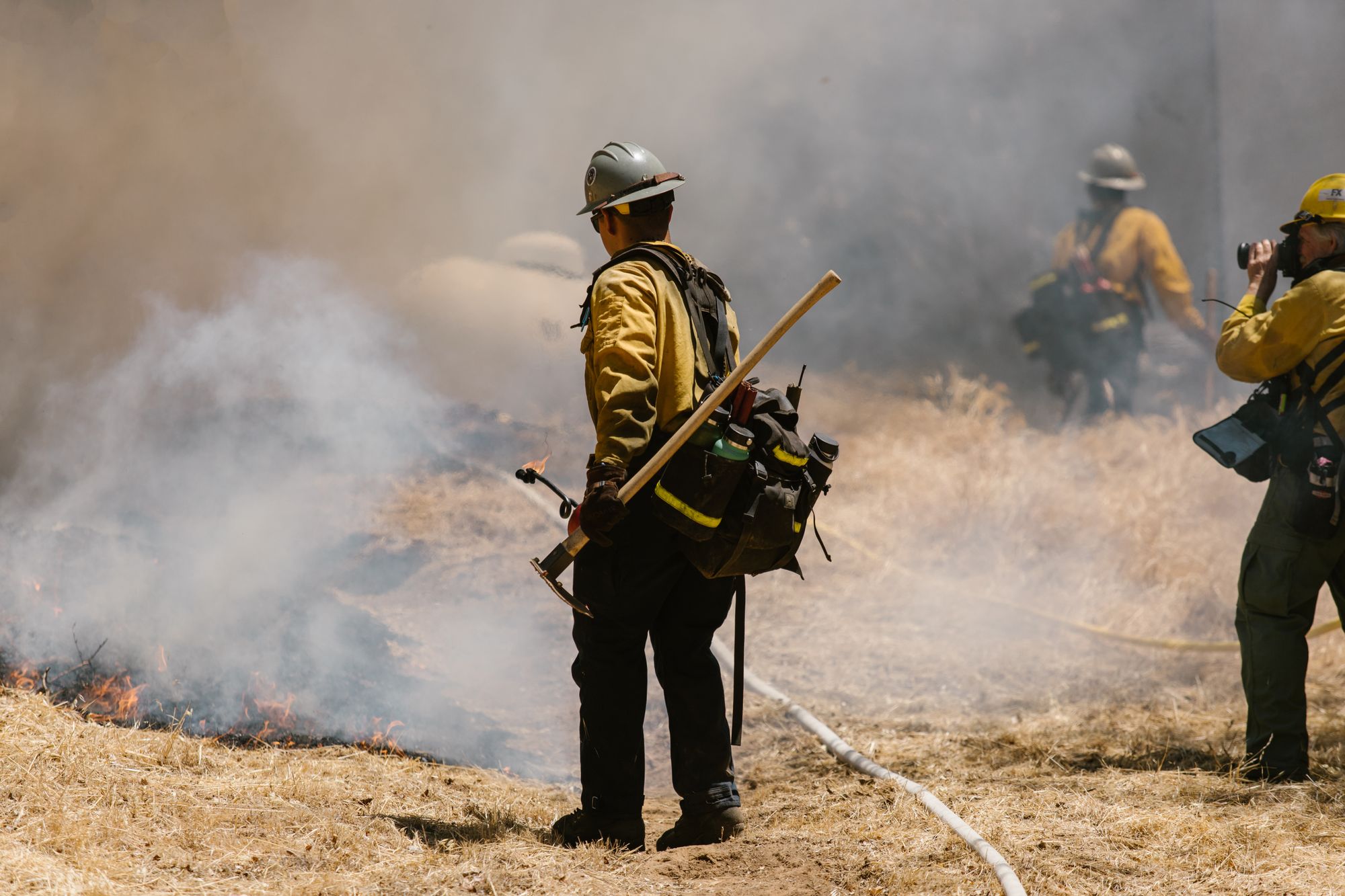 Brigadista forestal con herramienta de línea frente a un incendio de pastizal